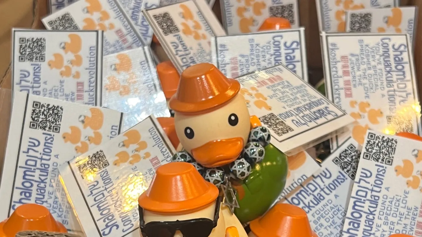 A warm cluster of Kosher Duck Revolution rubber ducks in little hats, glowing fairy lights behind them, gathered with their QR-code tags